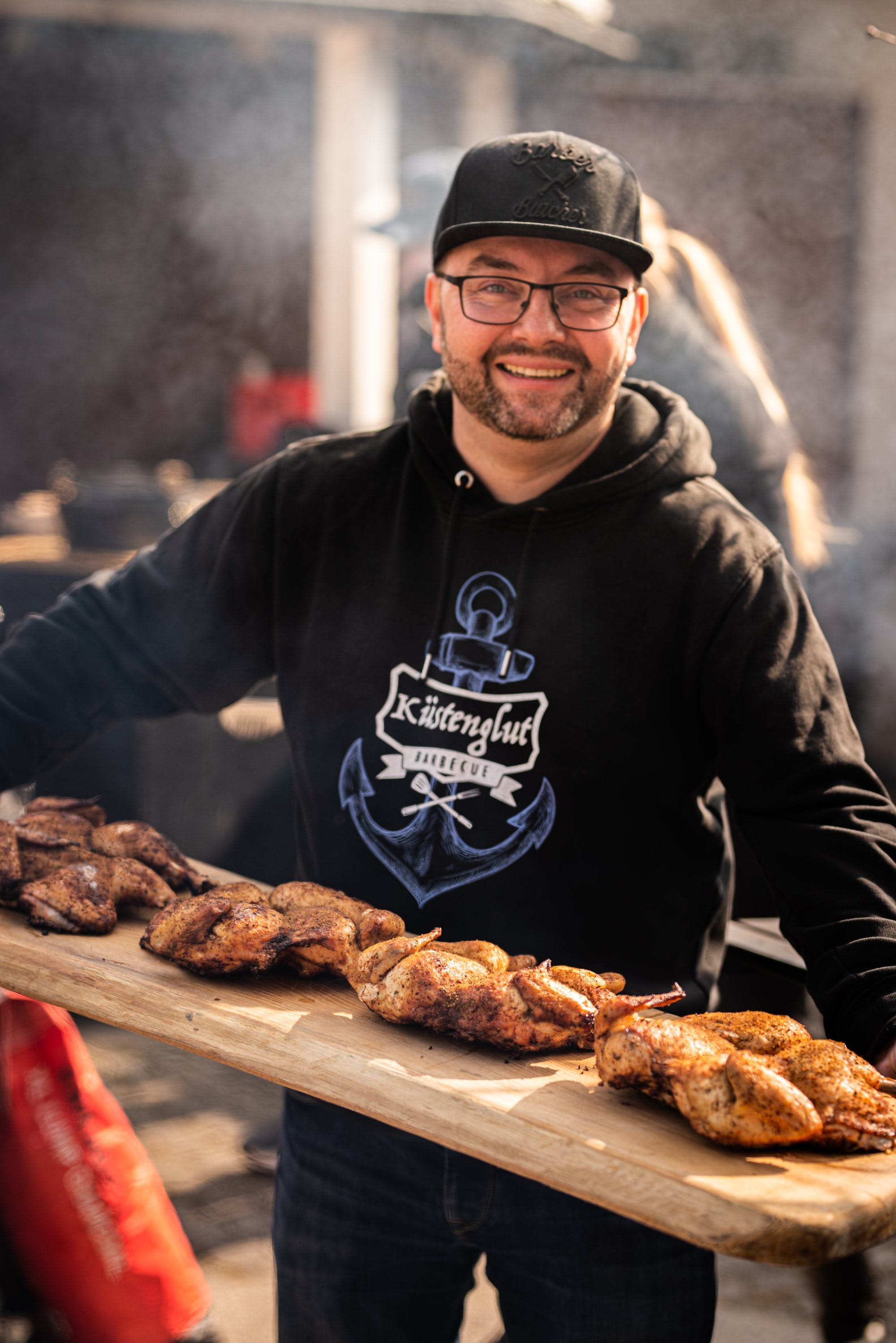 Sascha Lotzmann presenting finished grilled chicken on a wooden serving board